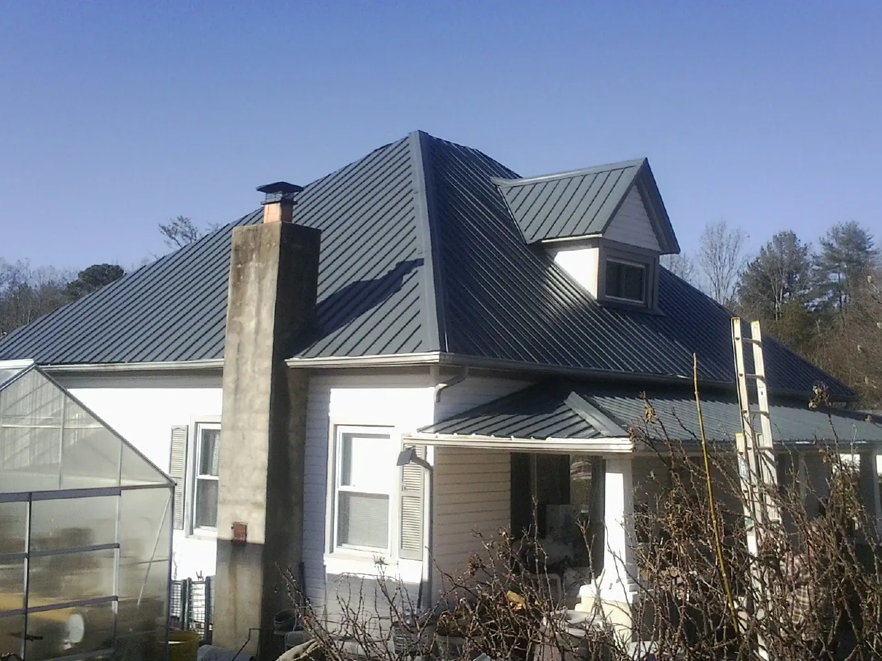 Dark blue standing seam metal roof on a white farmhouse with dormer — Slate & Tile Roof Repair by Roofing Brothers in Santa Clara