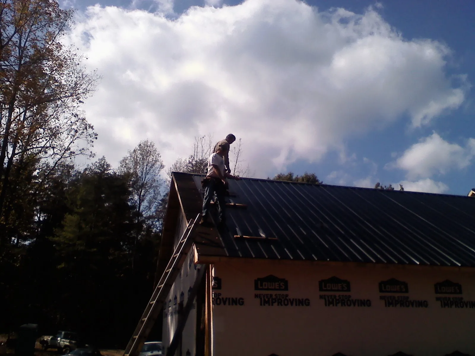 Roofer fastening dark metal panels high against a cloudy sky, from a Roof Inspection job in Santa Clara