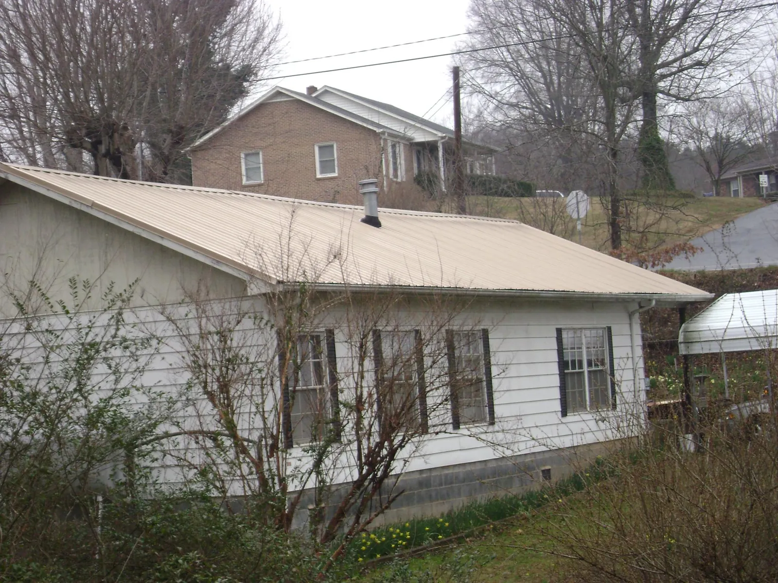 Tan metal roof on a white sided house set into a hillside — Commercial Roofing by Roofing Brothers in Santa Clara